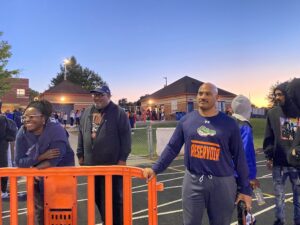 Coach Lewis and his companions staring in the distance near an orange gate on the track